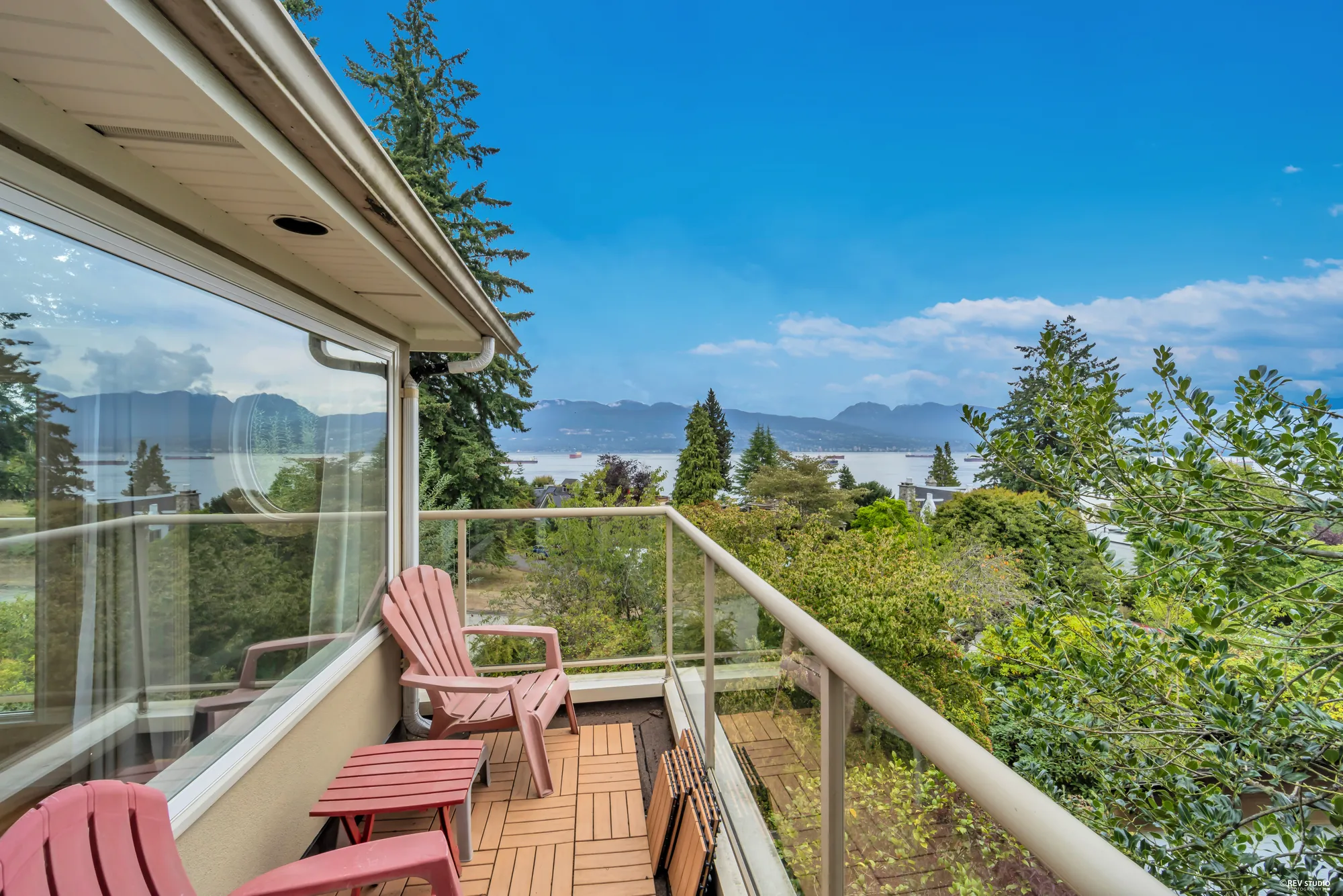 A balcony with two chairs, glass railing and the water beyond