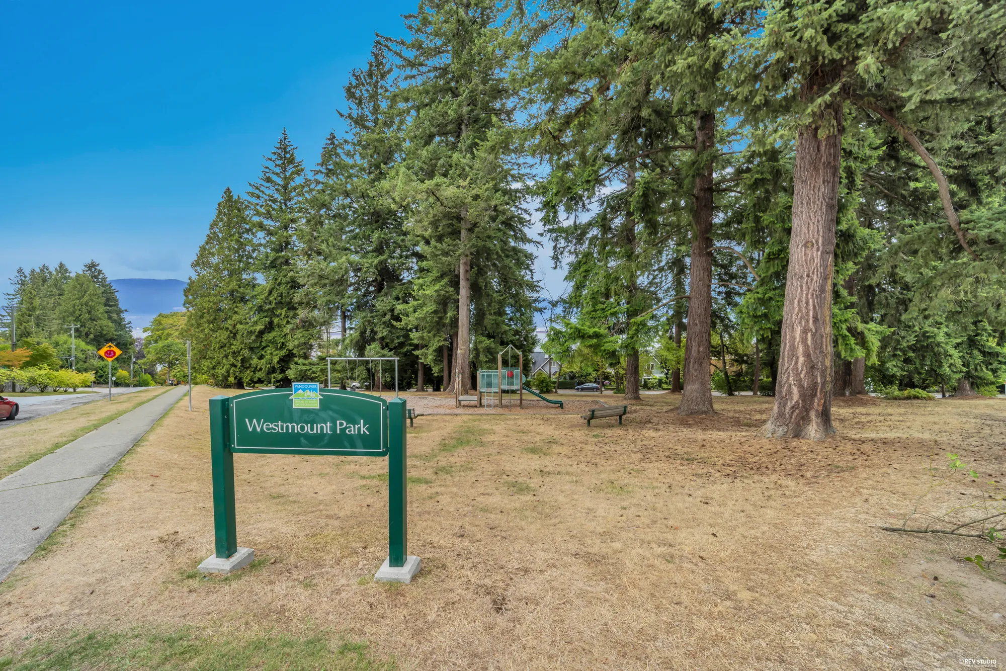 The Westmount Park sign across the street, with tall conifers behind it