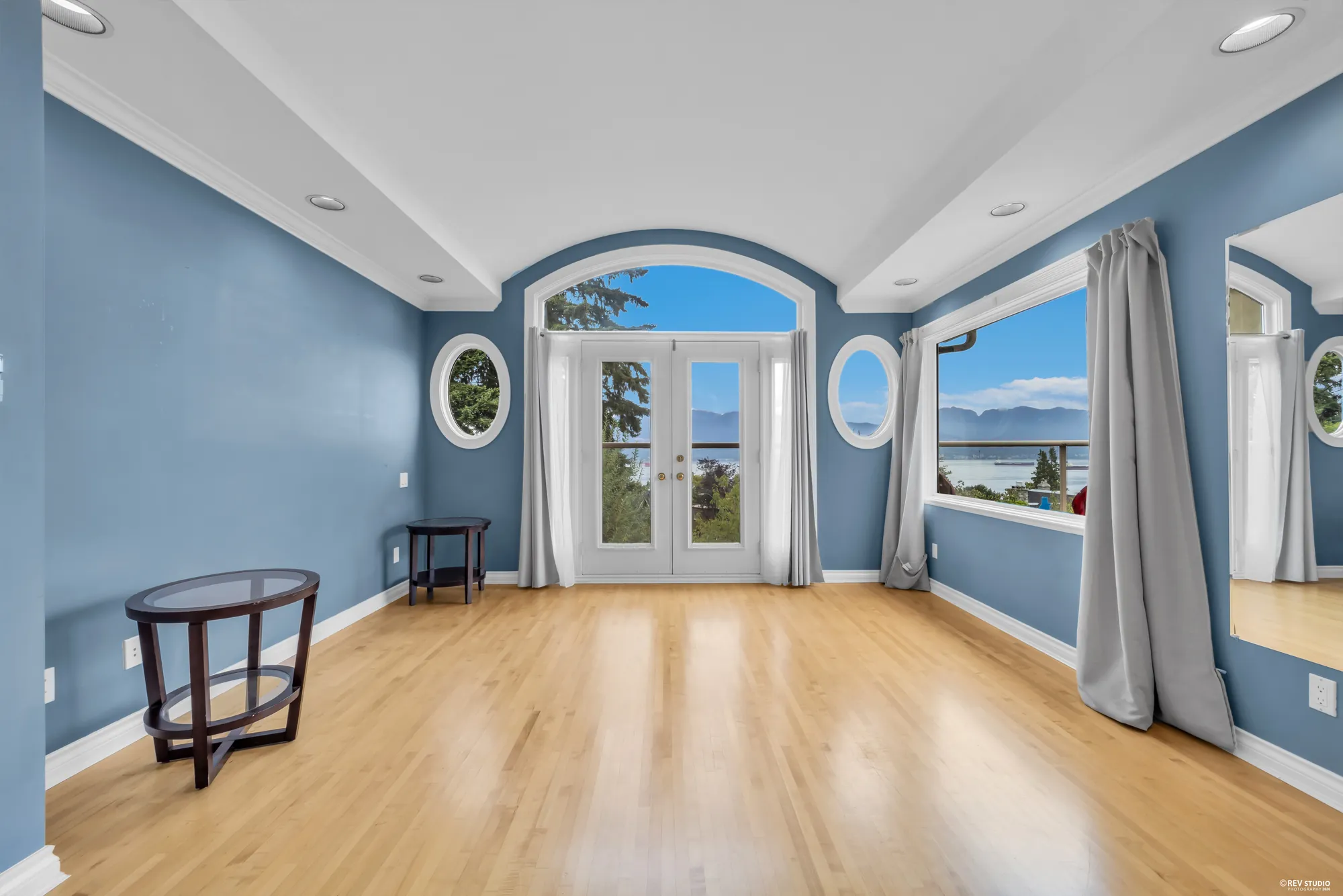 The primary bedroom as photographed, empty, with the arched balcony door and porthole windows